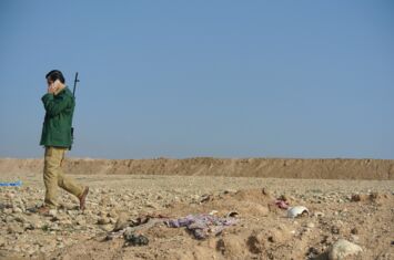 Ein bewaffneter telefoniert - Im Sand sind menschliche Überreste schwach zu erkennen