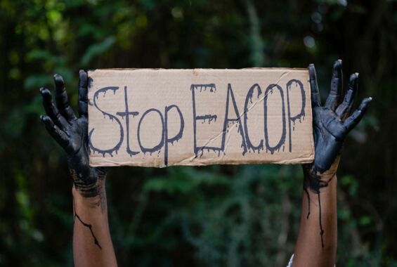 Stop EACOP Kampagne gegen die Rohölpipeline in Uganda und Tansania. Schwarz eingefärbte Hände halten ein Schild mit Stop EACOP hoch.