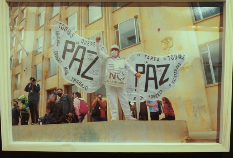 Foto einer Friedensaktivistin mit Flügeln und der Aufschrift PAZ in einer Ausstellung