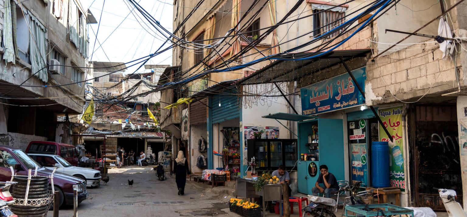 Verkabelung der Häuser sichtbar. Kleine Shops, Roller und Autos. Eine Straße in der palästinensischen Siedlung Burj al-Barajneh südlich von Beirut