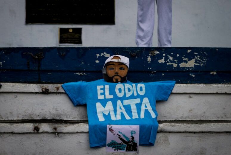 Ein blaues T-Shirt mit dem weißen Schriftzug "El Odio Mata - Hass tötet" liegt auf einer weißen Treppe. Darüber ist eine Maske von Präsident Bukele drapiert