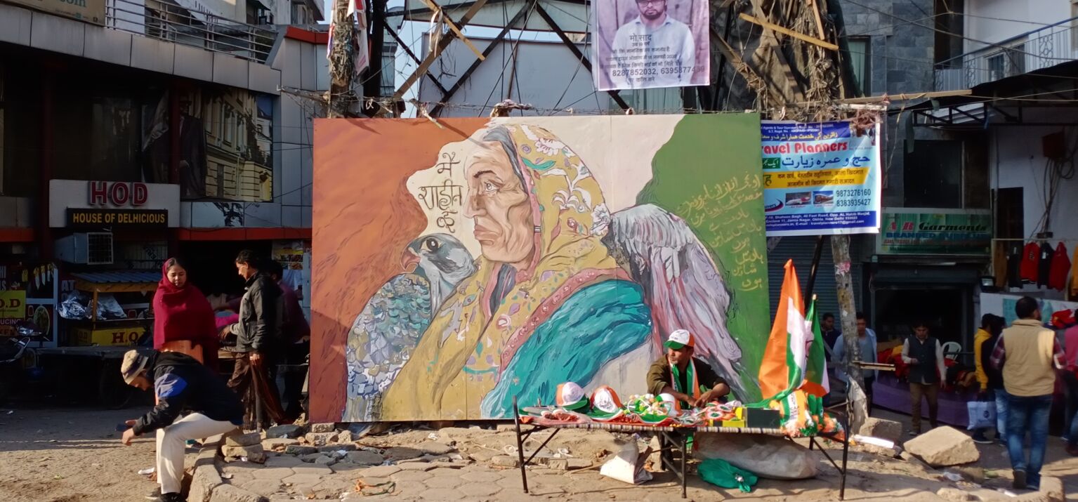 Große Malerei an einem Gerüst in den Straßen von Shaheen Bagh. Das Bild stellt eine ältere weibliche Person im Profil, nach links blickend mit einem Falken dar.