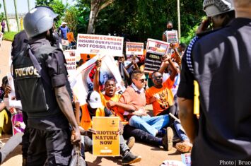 Proteste gegen die EACOP vor der chinesischen Botschaft in Uganda. Protestierende sitzend, umringt von Polizisten, halten Schilder in die Höhe