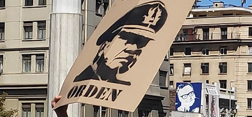 Es stehen Menschen auf der Straße und strecken ihre Arme in die Luft. Ein Plakat mit dem Foto Pinochets wird hochgehalten.