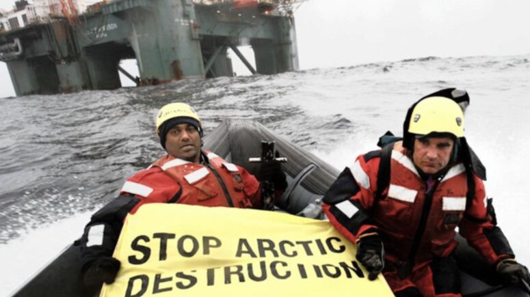 2 Männer, einer von ihnen Kumi Naidoo, mit dem Transparent Stop Arctic Destruction, vor einer Bohrinsel in der Arktischen See
