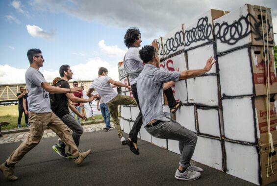 Menschen die gegen eine Mauer aus Kartons springen die eine Grenze symbolisiert