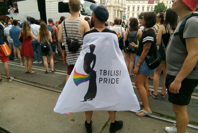 Das Logo der Tbilisi Pride auf der Europride Deomonstration in Wien prangt auf einem Banner, das wie ein Superheld*innenumhang getragen wird