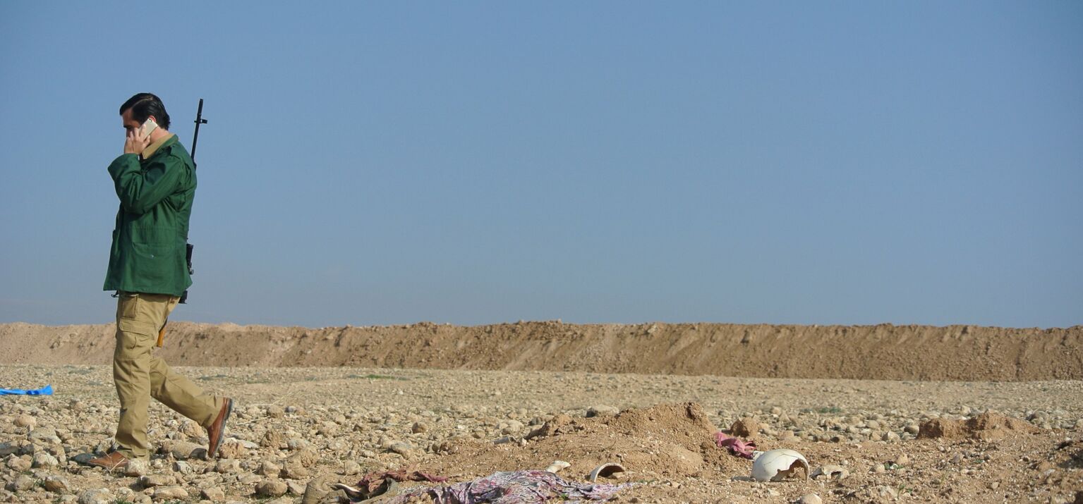 Ein bewaffneter telefoniert - Im Sand sind menschliche Überreste schwach zu erkennen