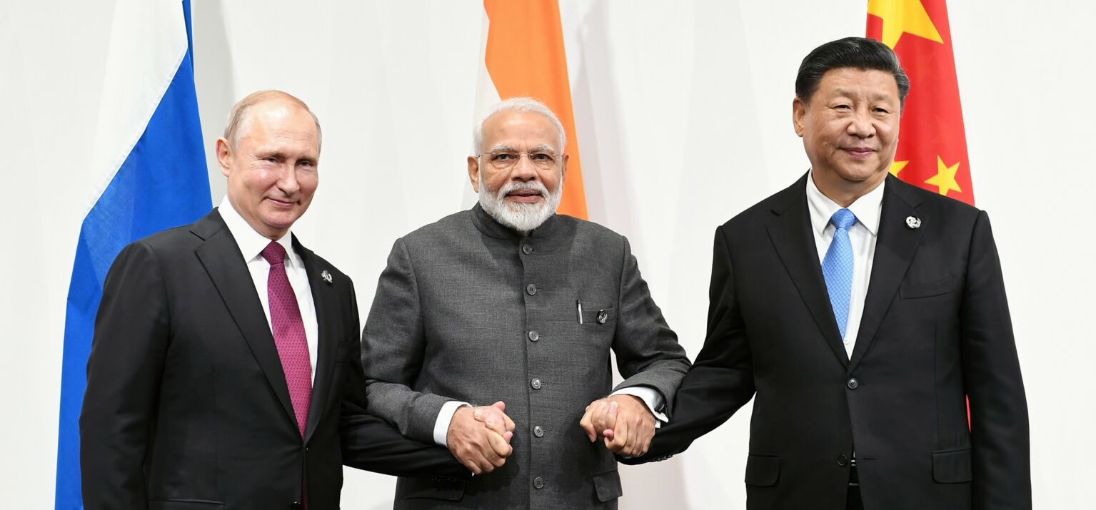 Narendra Modi in der Mitte hält Wladimir Putin (links) und Xi Jingping (rechts) an der Hand, im Hintergrund die Landesflaggen