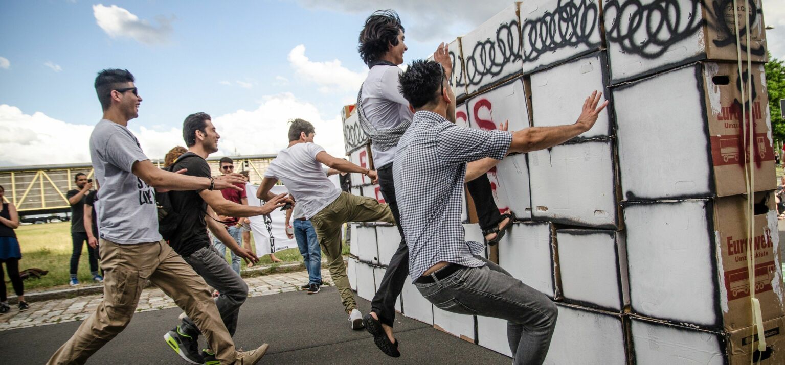 Menschen die gegen eine Mauer aus Kartons springen die eine Grenze symbolisiert