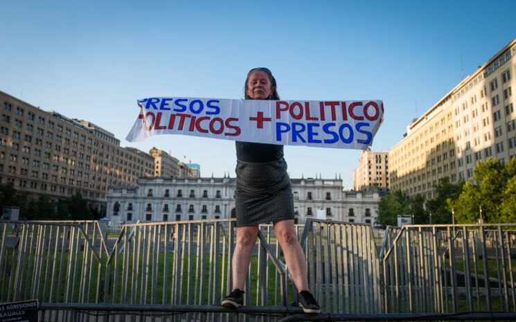 Frau mit einem Banner auf einer Absprerrung vor dem Palast La Moneda in Santiago de Chile