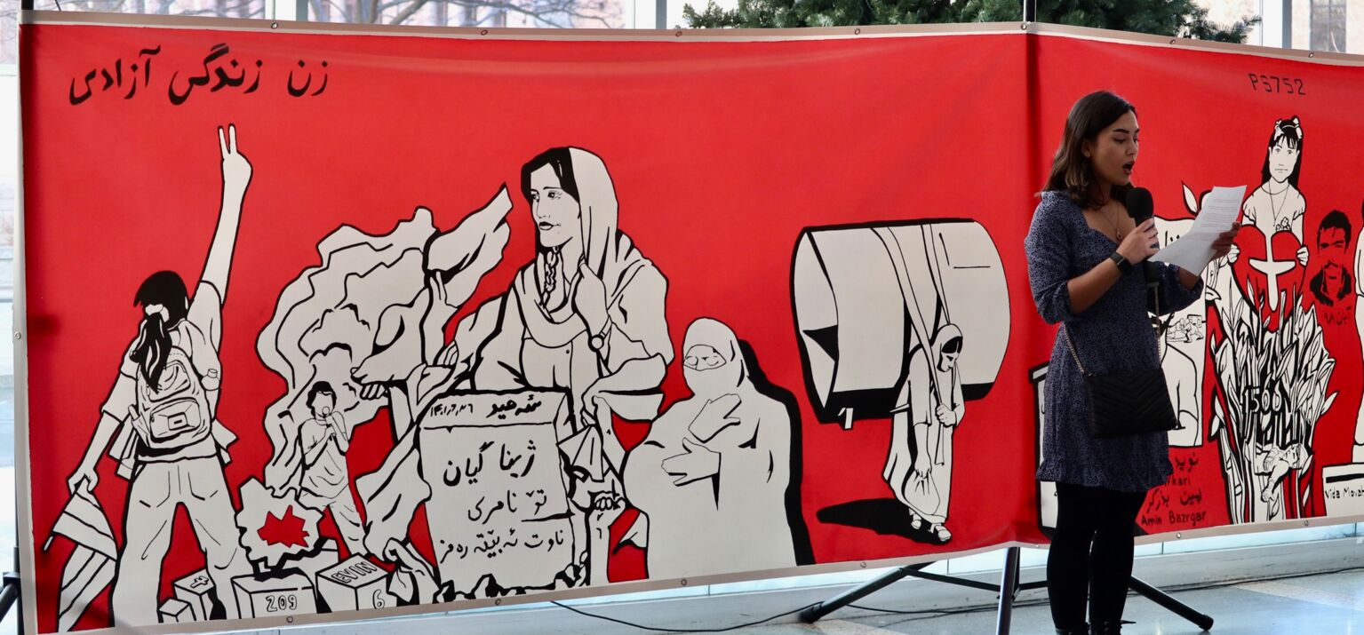 Graffiti Wand mit Motiven des Protestes, im Vordergrund eine Rednerin