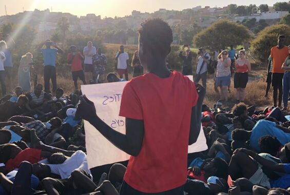 Erinnerung an das Massaker von Melilla: Menschen liegen auf dem Boden, eine Person hält ein Plakat.