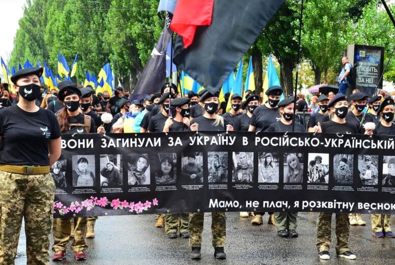 Viele Frauen demonstrieren in Uniform und mit ukrainischen Flaggen, sie halten ein schwarzes Banner, auf dem Fotos getöteter Soldatinnen zu sehen sind.