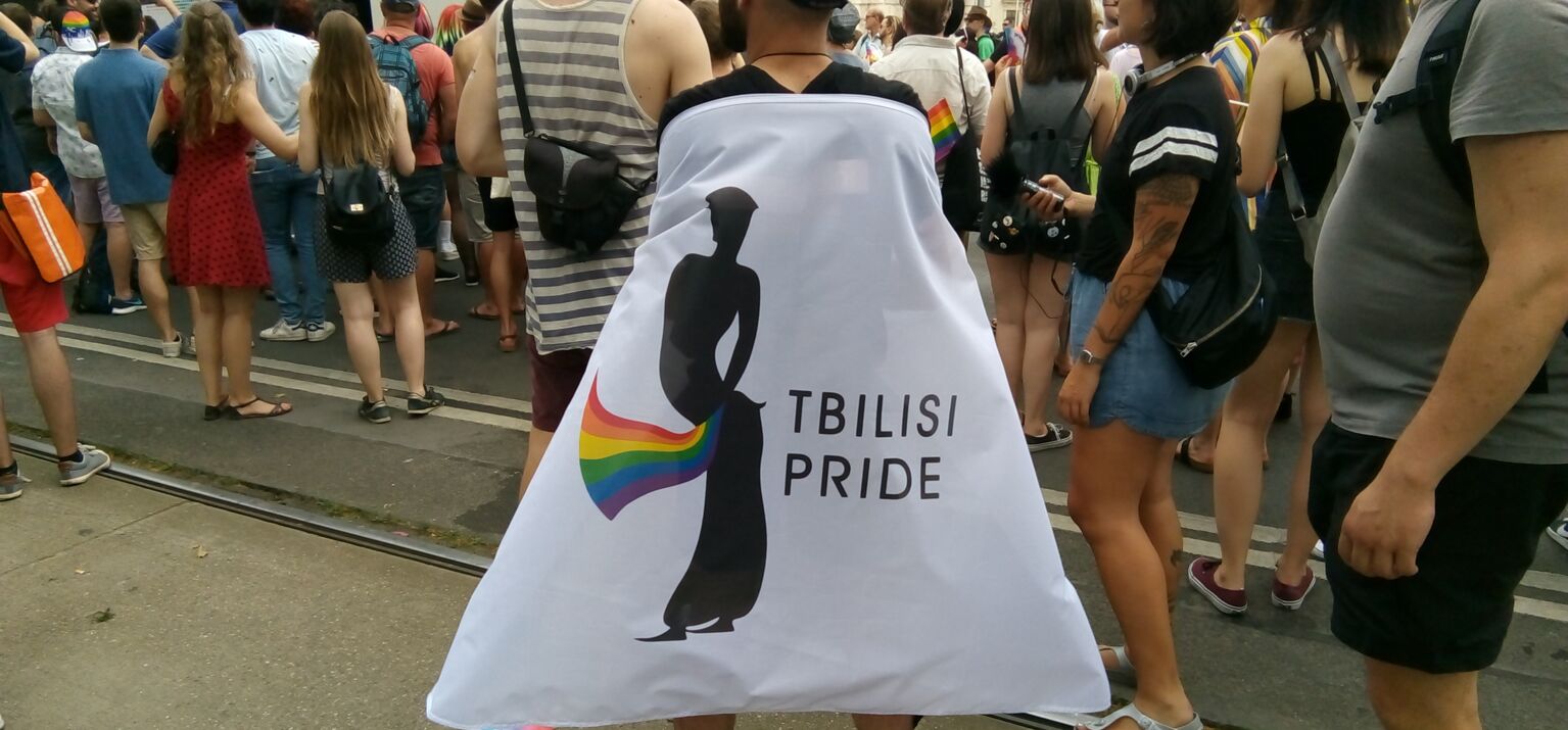 Das Logo der Tbilisi Pride auf der Europride Deomonstration in Wien prangt auf einem Banner, das wie ein Superheld*innenumhang getragen wird