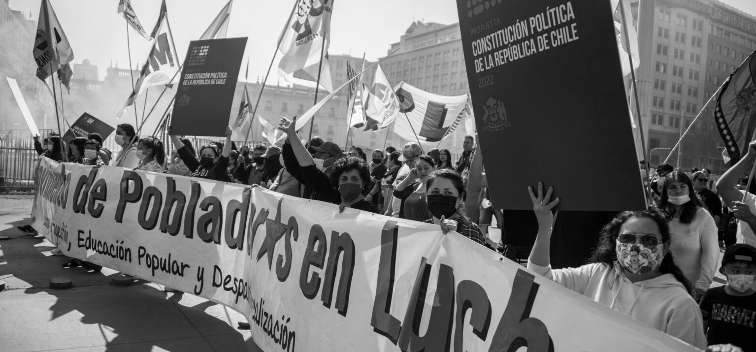 Ein Protest der Anhänger*innen des neuen Verfassungsentwurfs in Santiago, Chile. Menschen mit Fahnen und Schildern hinter einem langen Transparent sind zu sehen.