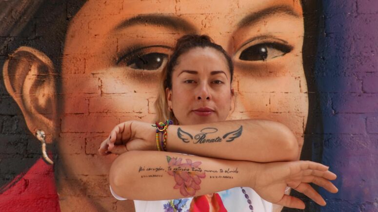 Portrait einer Frau mit Tatoos auf dem Arm und einem Murales im Hintergrund