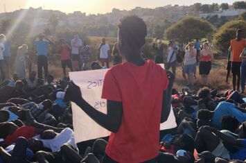 Erinnerung an das Massaker von Melilla: Menschen liegen auf dem Boden, eine Person hält ein Plakat.