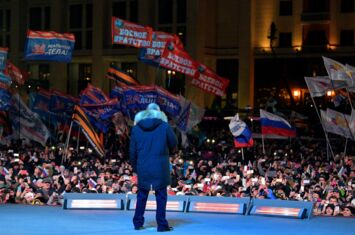 Der russische Präsident Wladimir Putin steht auf einer Bühne, Anhänger*innen schwenken Russland-Fahnen