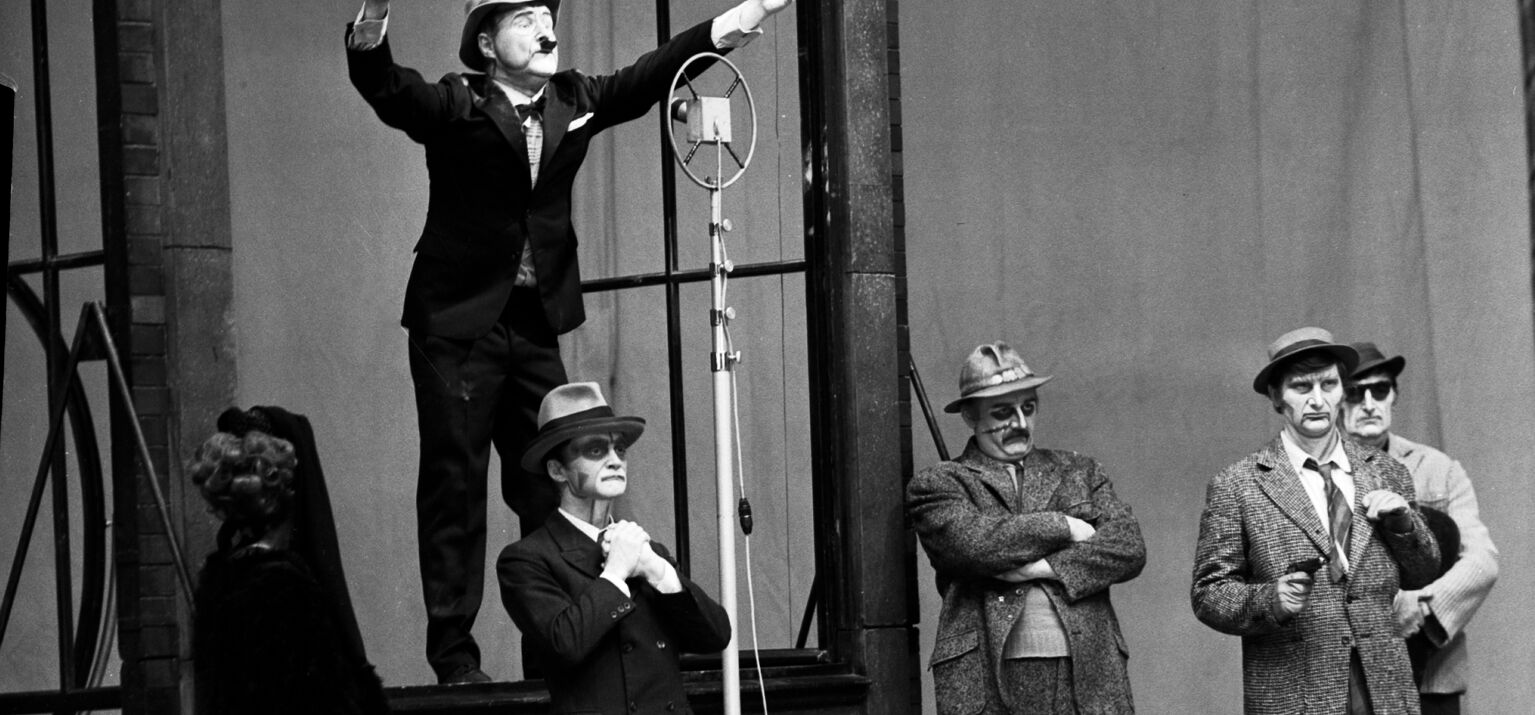 5 Männer auf einer Theaterbühne - einer spricht in eine Mikrofon - aus: »Der aufhaltsame Aufstieg des Arturo Ui«