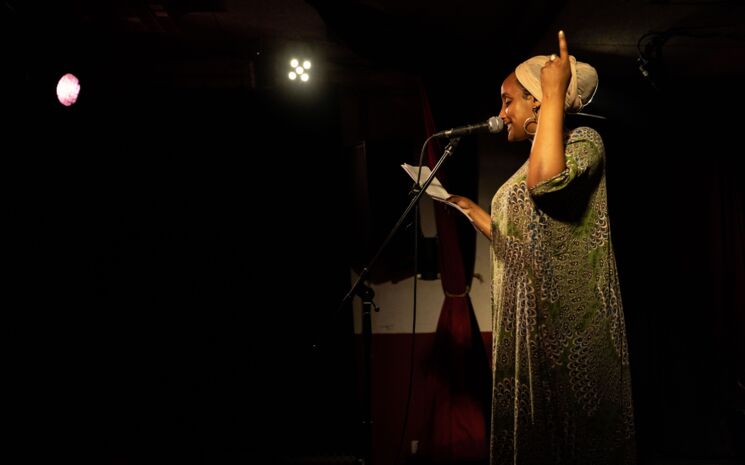 Furat Abdulle steht auf vor einem Mikrofon im Scheinwerferlicht und trägt einen Text vor, dabei zeigt sie zur Decke. | Foto: Sévérine Kpoti