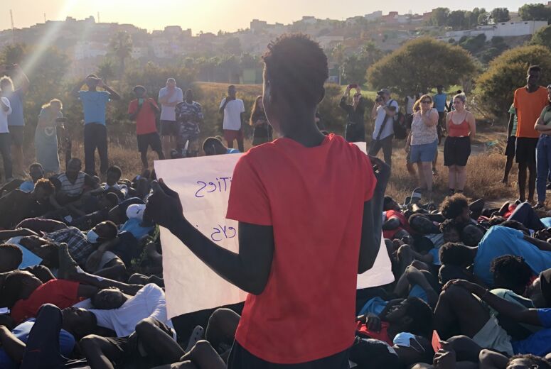 Erinnerung an das Massaker von Melilla: Menschen liegen auf dem Boden, eine Person hält ein Plakat.