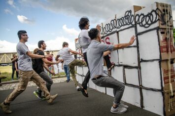 Menschen die gegen eine Mauer aus Kartons springen die eine Grenze symbolisiert