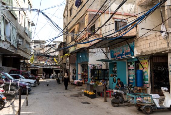 Verkabelung der Häuser sichtbar. Kleine Shops, Roller und Autos. Eine Straße in der palästinensischen Siedlung Burj al-Barajneh südlich von Beirut
