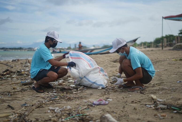 Zwei Menschen von OCG Saving The Ocean sammeln Müll am Strand von Bali