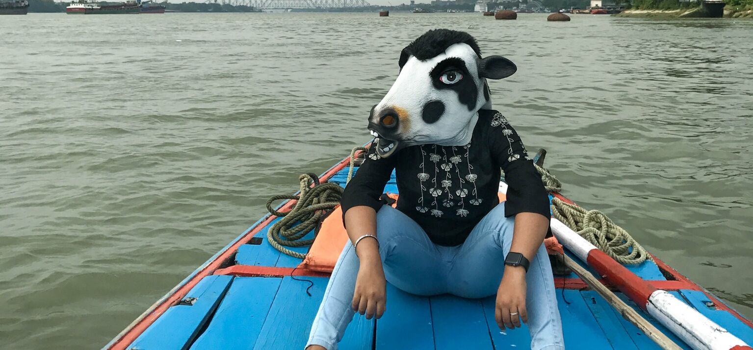 Person mit einer Maske einer heiligen Kuh auf einem Boot