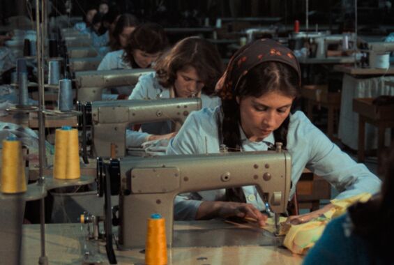 Filmstill aus »Kara Kafa«. Frauen in blauen Uniformen sitzen in einer Reihe über Nähmaschinen gebeugt.